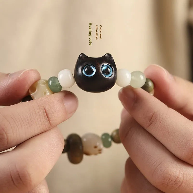 Hand-woven bracelet with jade, bodhi, and guajacwood beads, a multi-treasure cube, and a carved cat's paw charm.