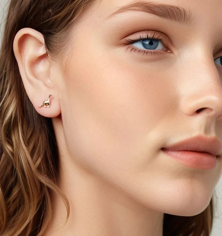 Asymmetric dinosaur stud earrings in 925 silver, animal element design, gold or silver colour option, on a neutral background