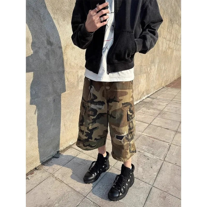 Man wearing loose straight-cut camouflage jeans with patch ripped detailing and a cropped ankle length.