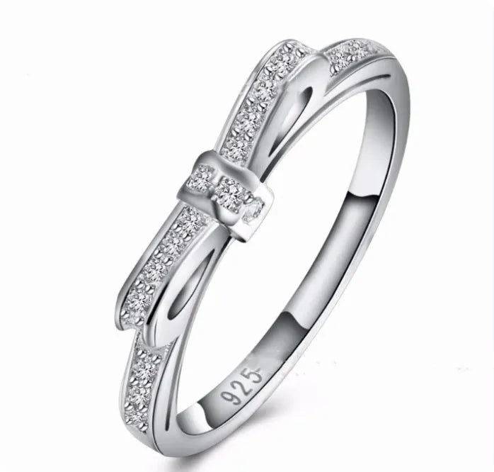 Silver bow-shaped ring set with clear rhinestone and zircon crystals on a model's hand.