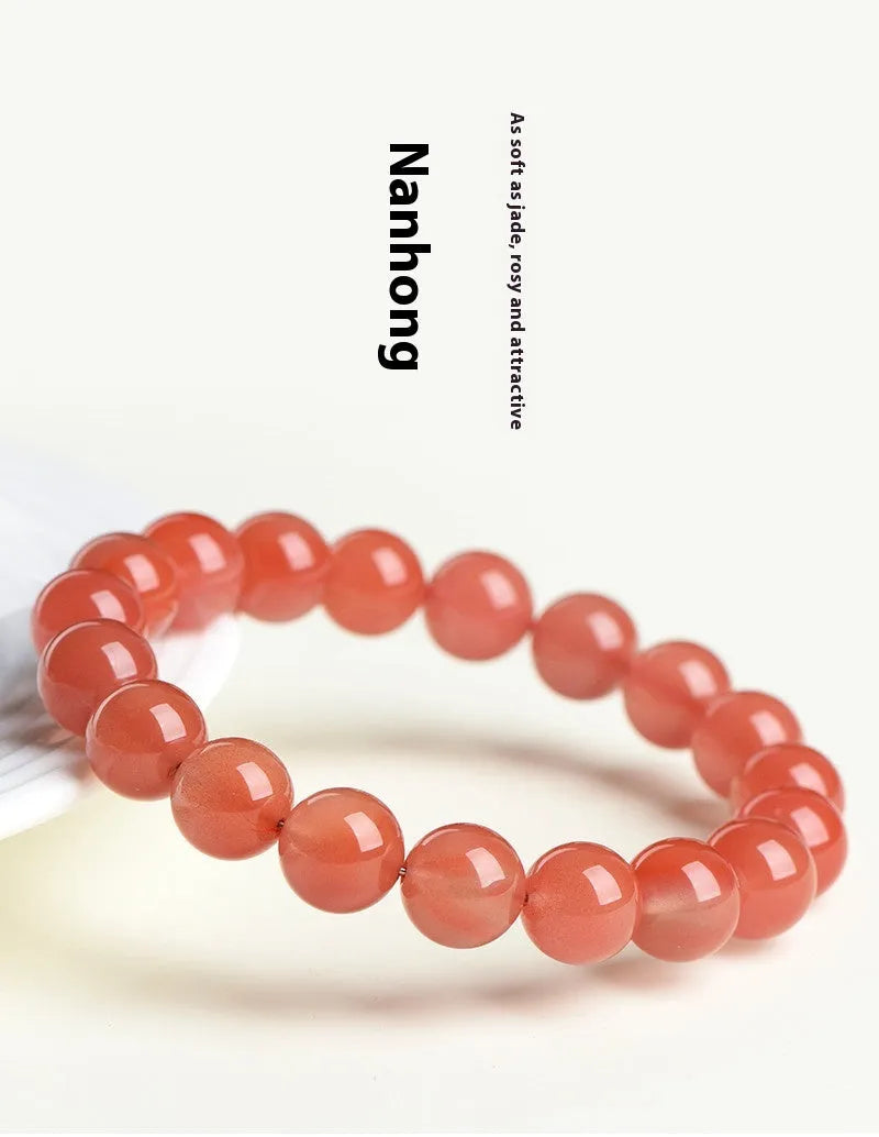 Scattered polished cherry red agate beads and elastic cord for a DIY bracelet next to an assembled single-strand bracelet.