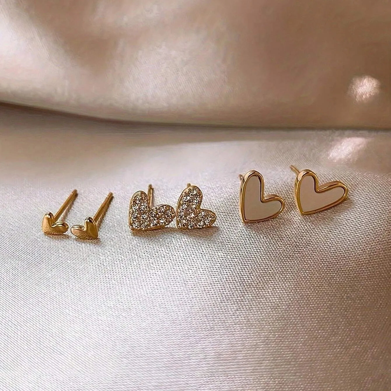 Three pairs of heart-shaped alloy earrings in gold, black, black and white, and pink electroplated colours