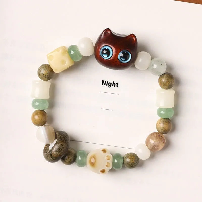 Hand-woven bracelet with jade, bodhi, and guajacwood beads, a multi-treasure cube, and a carved cat's paw charm.