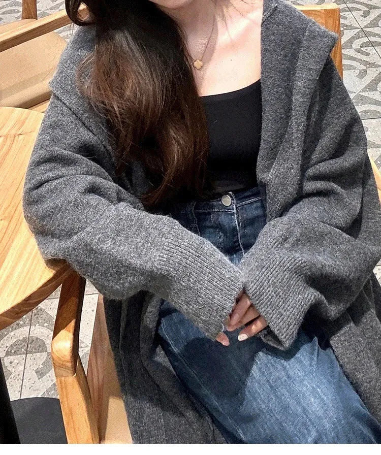 A woman wearing a long, loose, hooded knitted cardigan in a solid colour, demonstrating its below-the-knee length.
