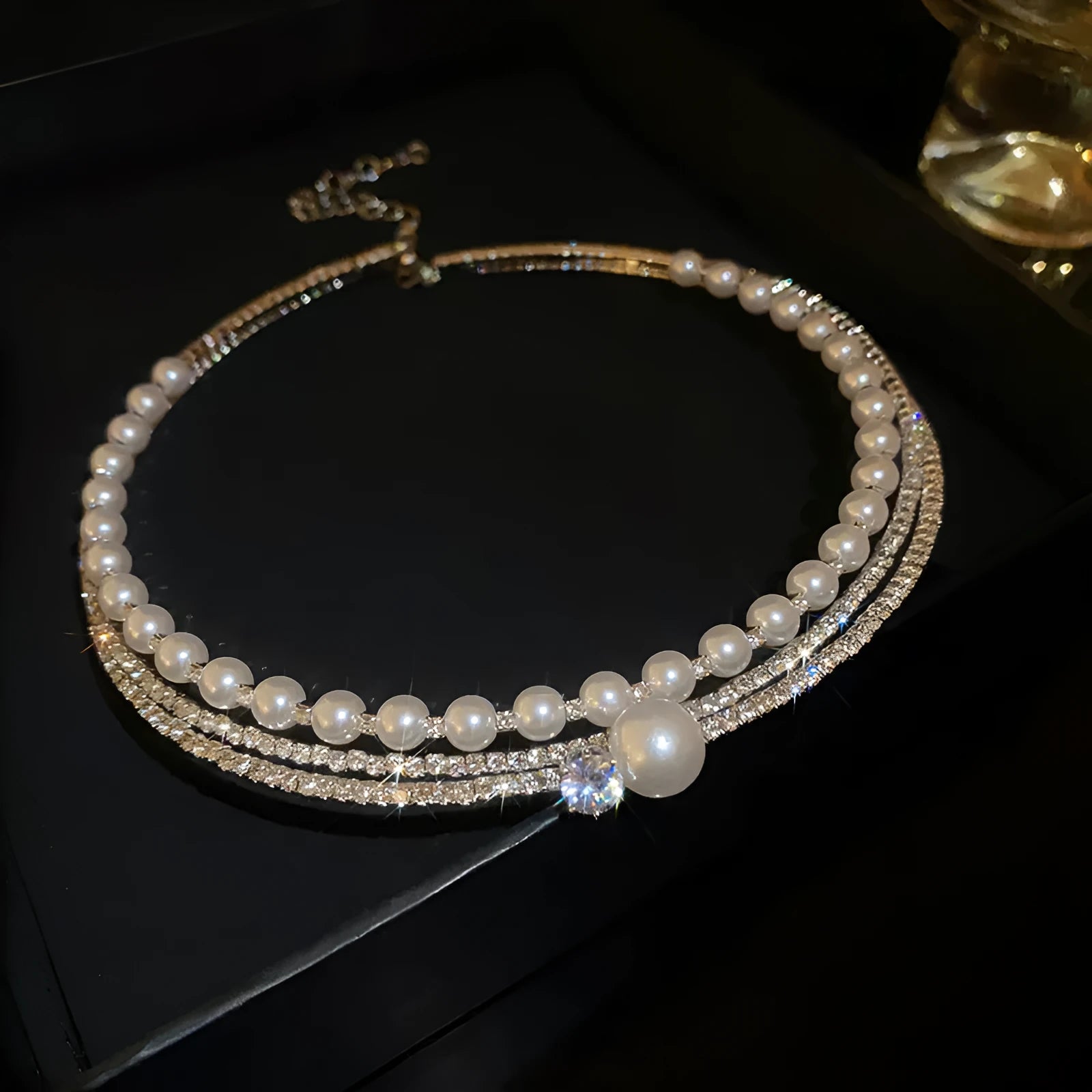 Close-up of a silver curved geometric collar necklace with a ball pendant, resting on a surface.