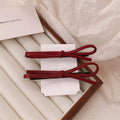 A wine red leather hair clip with a bow design, shown as a single barrette.