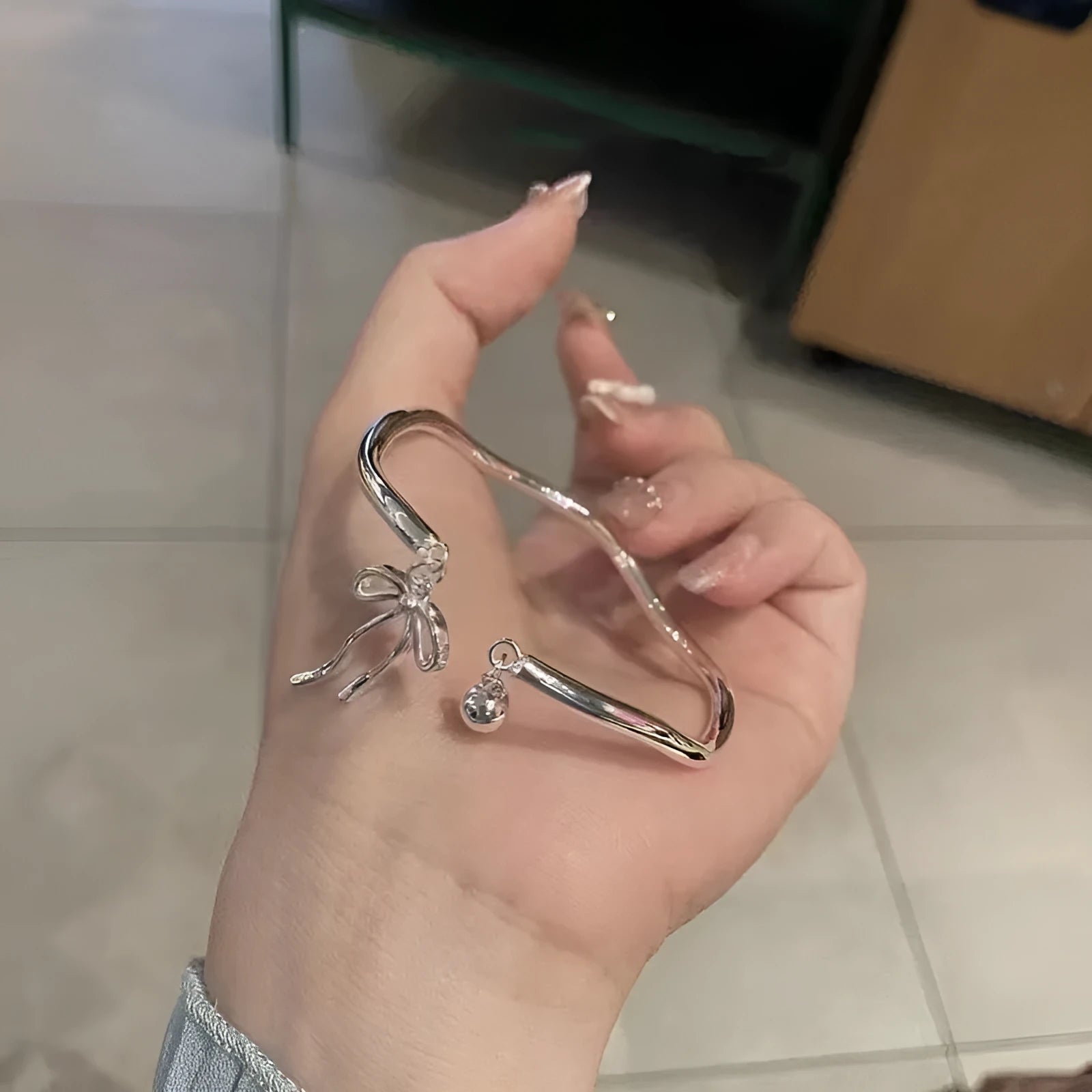 Silver bow coloured adjustable zinc alloy bracelet with an opening bow bell design.