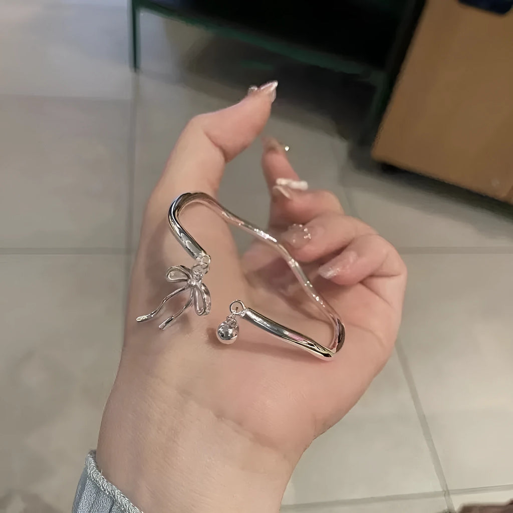 Silver coloured adjustable bracelet with a bow and bell charm on a chain.