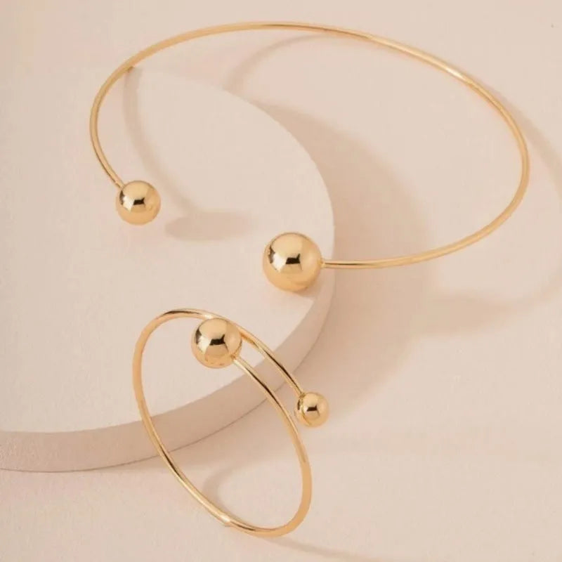 Gold dislocation ball open-end thin bangle bracelet with matching necklace on a flat surface