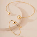 Gold dislocation ball open-end thin bangle bracelet with matching necklace on a flat surface