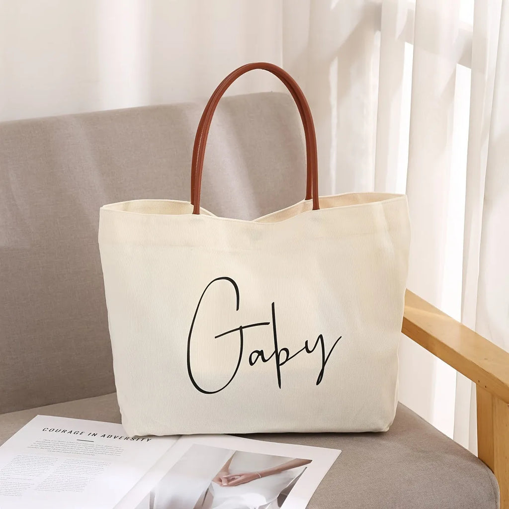 Beige white canvas tote bag with top handles and an internal zip pocket, shown with a book and keys.