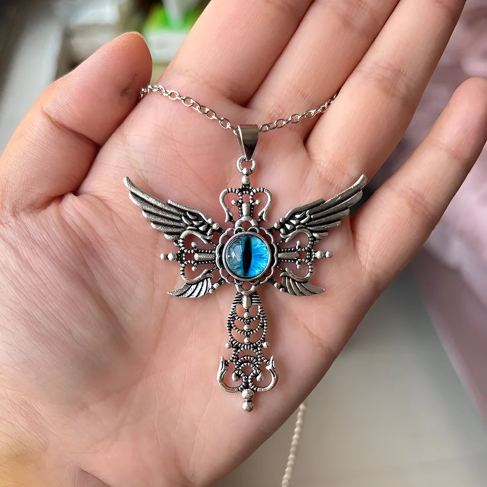 Close-up of a colourful alloy necklace featuring a geometric pendant with devil wings and a cross design.