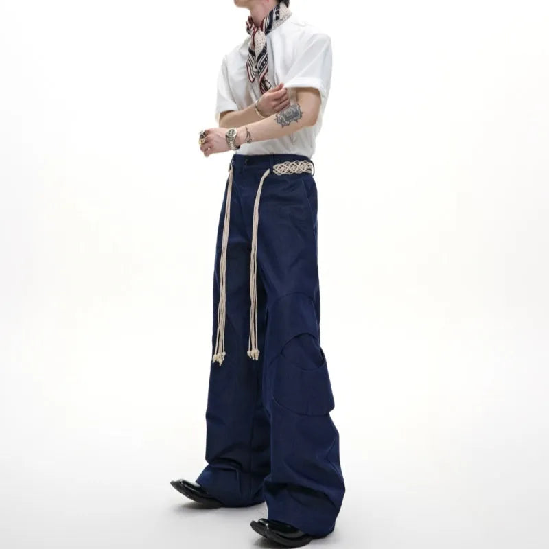 Men's dark coloured loose-fit straight-leg cotton trousers with decorative tassel and pocket zipper details.