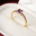 Colourful hexagon zircon copper ring in gold and gun black finishes on a size guide.