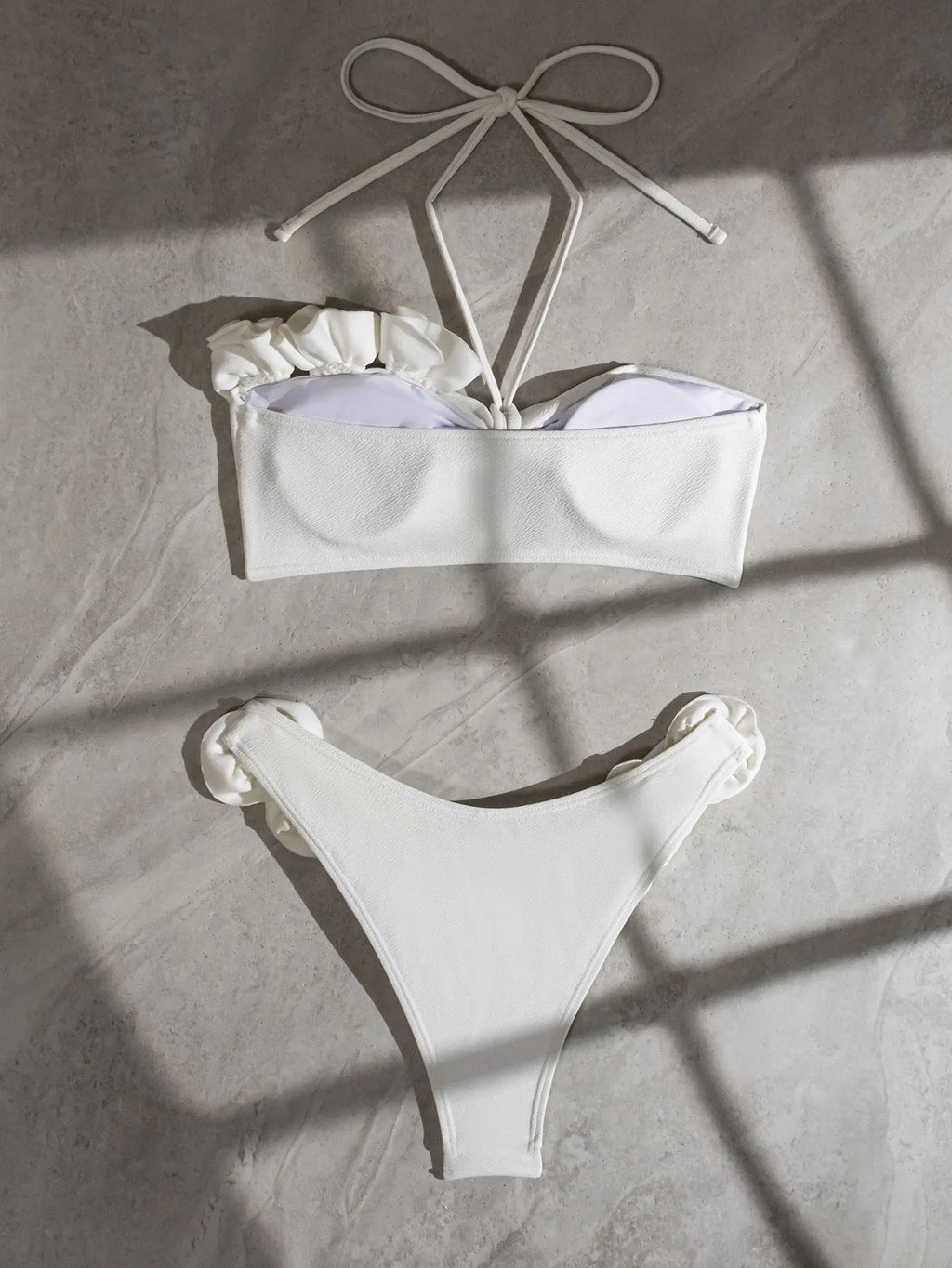White halter bikini with lace-up front and three-dimensional floral detail on a mannequin.