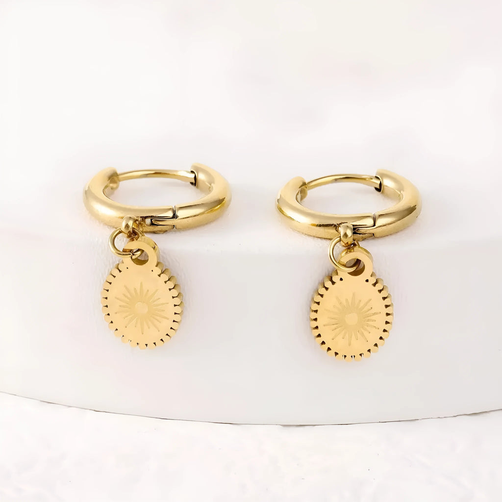 A pair of stainless steel geometric earrings featuring a central ellipse design on a woman's ear.