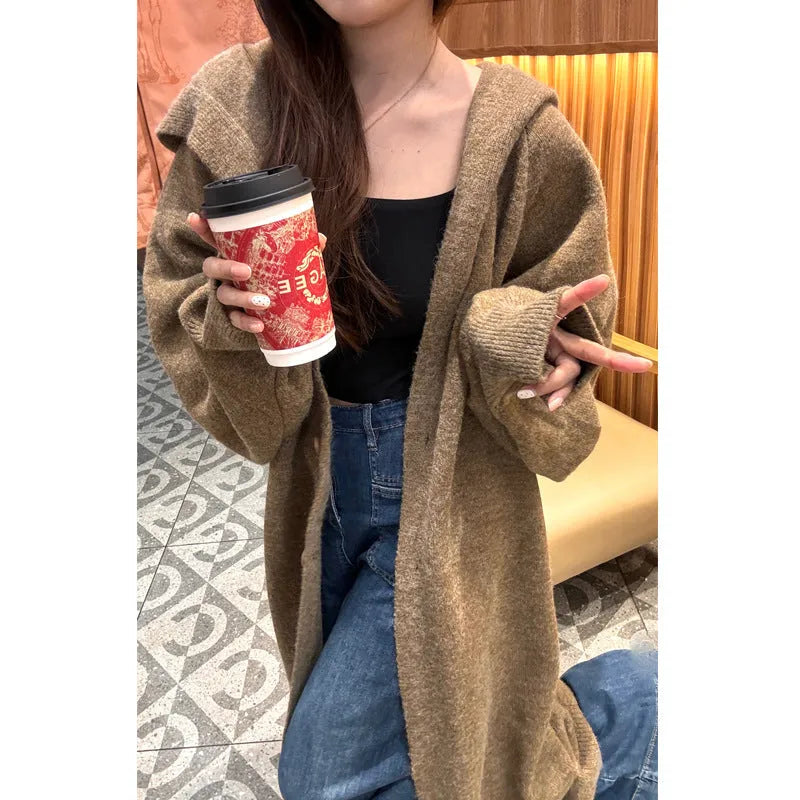 A woman wearing a long, loose, hooded knitted cardigan in a solid colour, demonstrating its below-the-knee length.