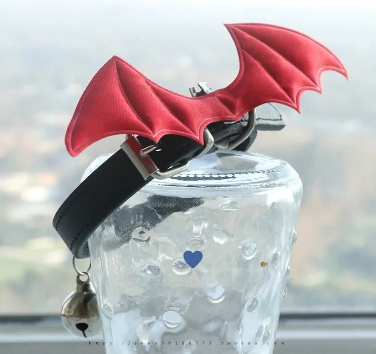 Small black patent leather pet collar with silver devil wings charm and bell on a white background.