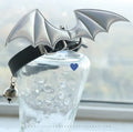 Small black patent leather pet collar with silver devil wings charm and bell on a white background.