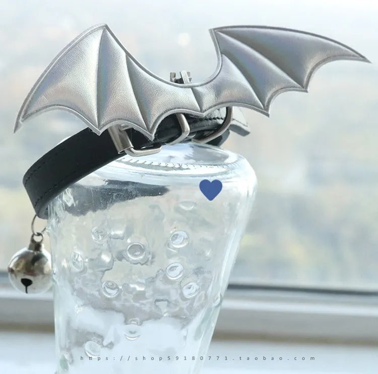 Small black patent leather pet collar with silver devil wings charm and bell on a white background.