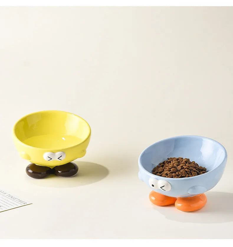 Blue and yellow ceramic slanted pet food bowls with animal face expressions for cervical spine support.