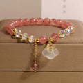 Women's bracelet with strawberry quartz and white agate beads and metal auspicious cloud charms on a white background.