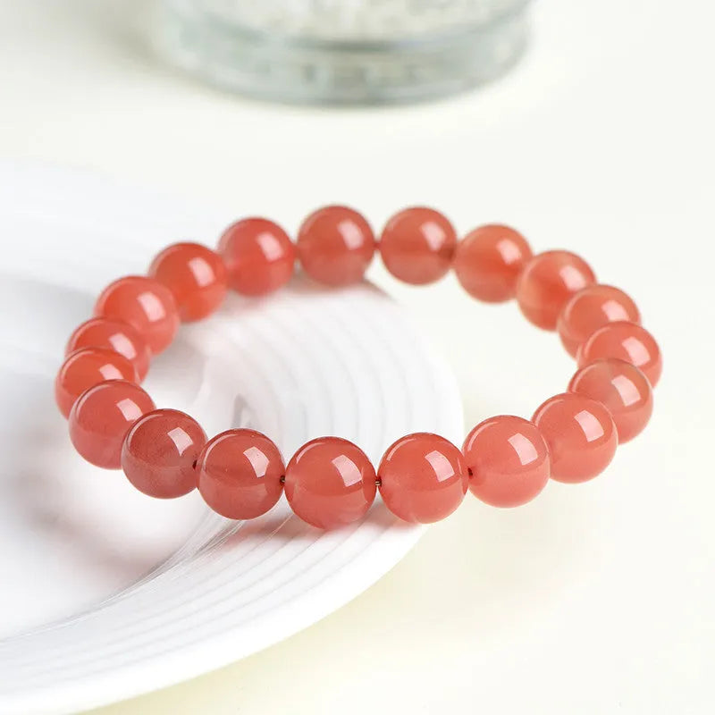 Scattered polished cherry red agate beads and elastic cord for a DIY bracelet next to an assembled single-strand bracelet.