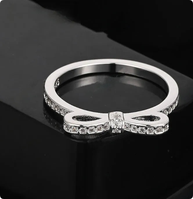 Silver bow-shaped ring set with clear rhinestone and zircon crystals on a model's hand.