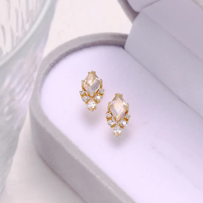 A pair of geometric shaped silver ear studs with sweet white crystal centres on a plain background.
