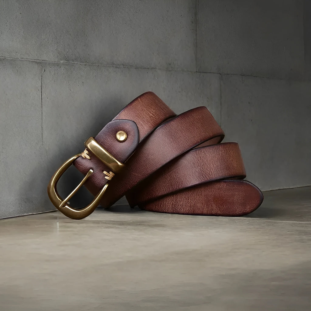 Men's black casual leather belt with copper pin buckle on a jeans background.
