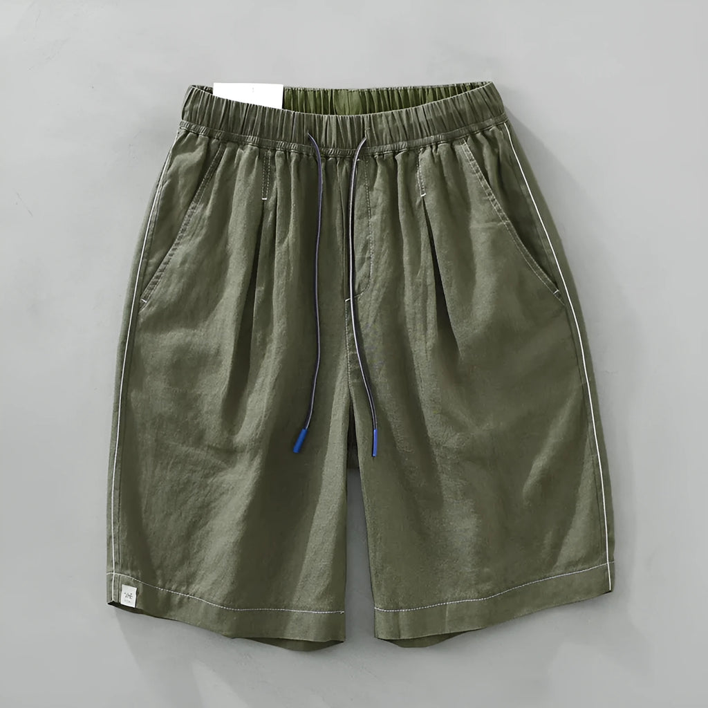 Man wearing loose green linen shorts with a drawstring waist and straight leg cut.
