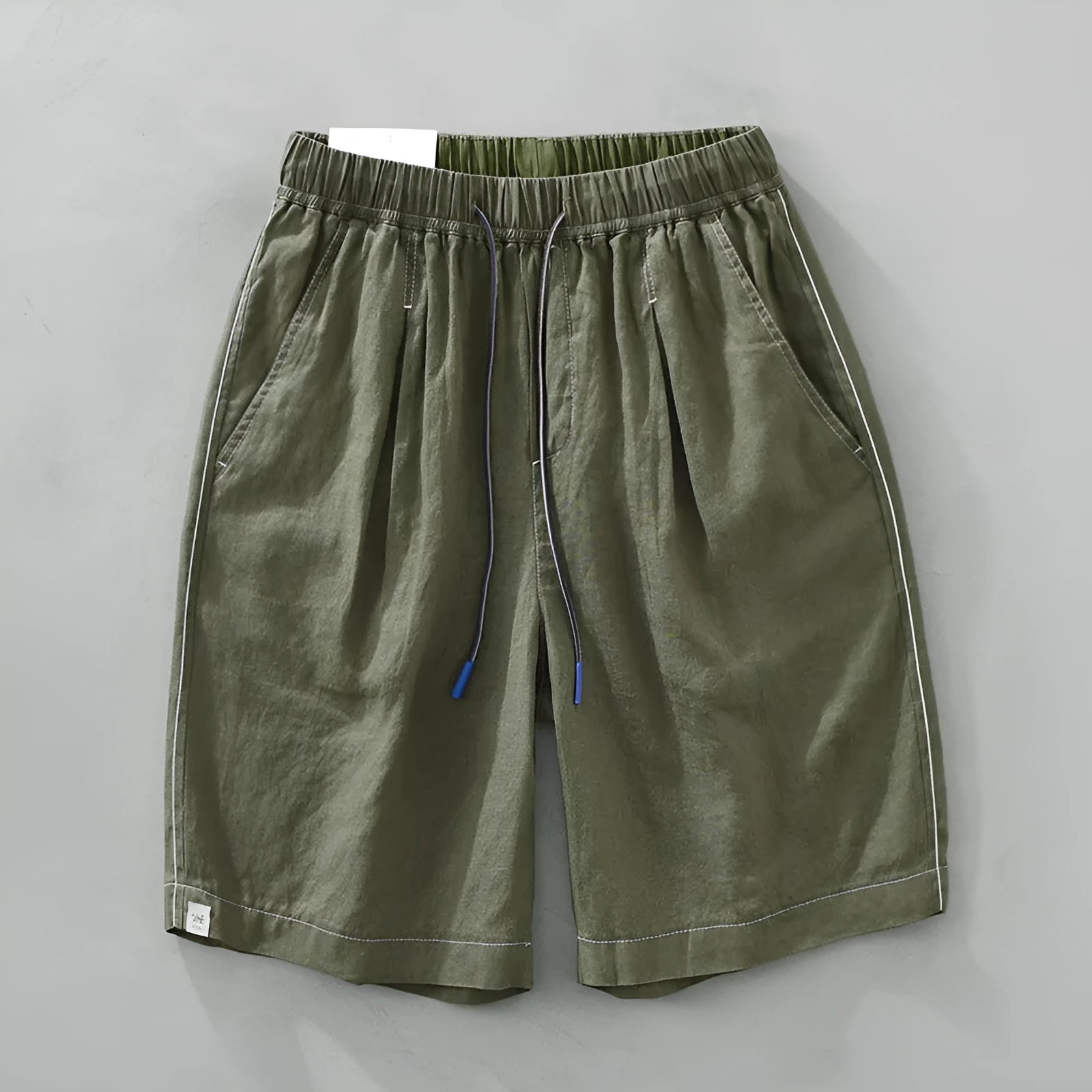 Man wearing loose green linen shorts with a drawstring waist and straight leg cut.