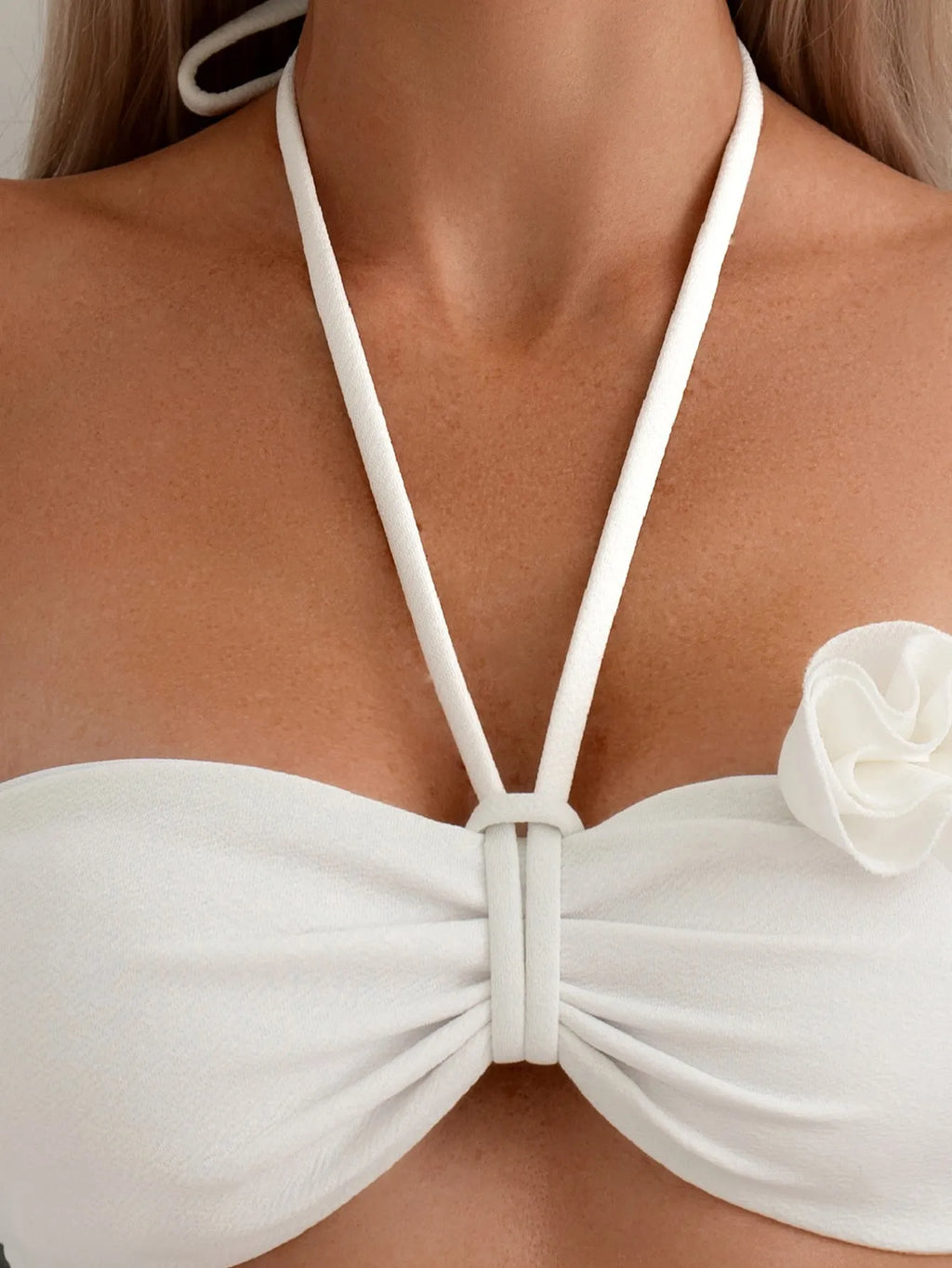 White halter bikini with lace-up front and three-dimensional floral detail on a mannequin.