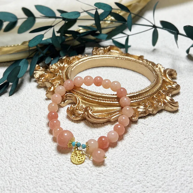 A simple pink natural stone and alloy bracelet with an adjustable clasp on a wrist.