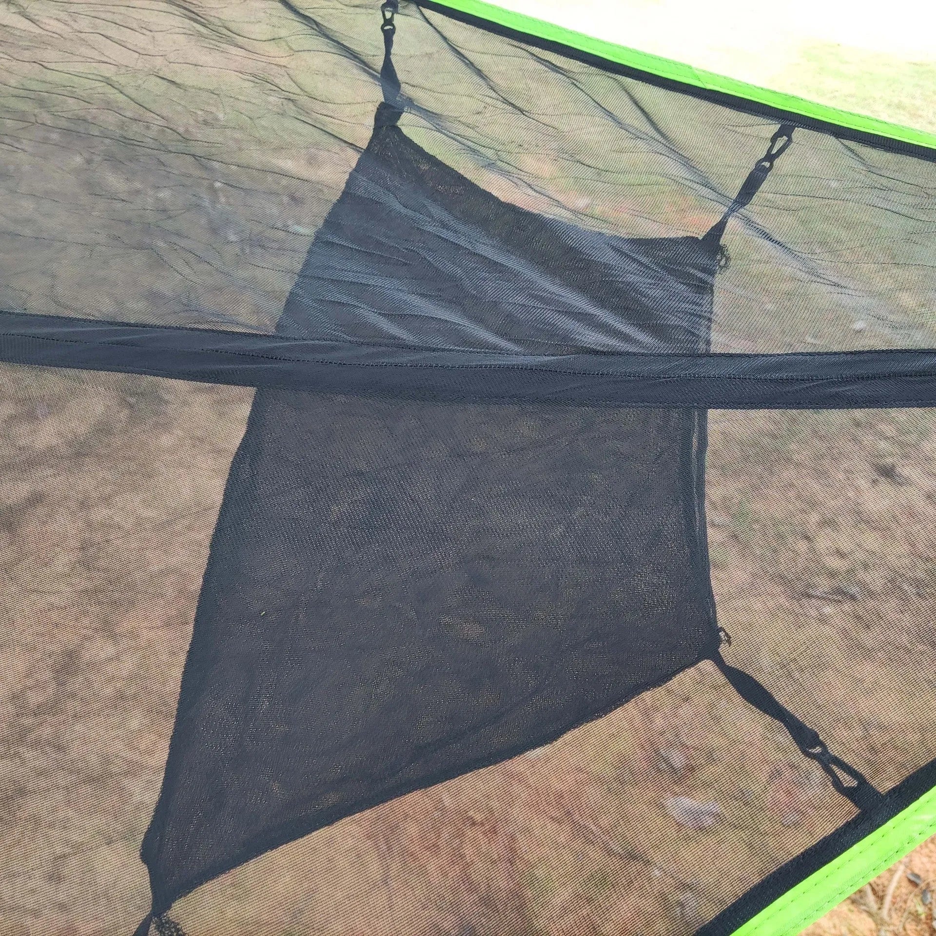 Folding portable mesh hammock in black, set up outdoors, with three supporting straps