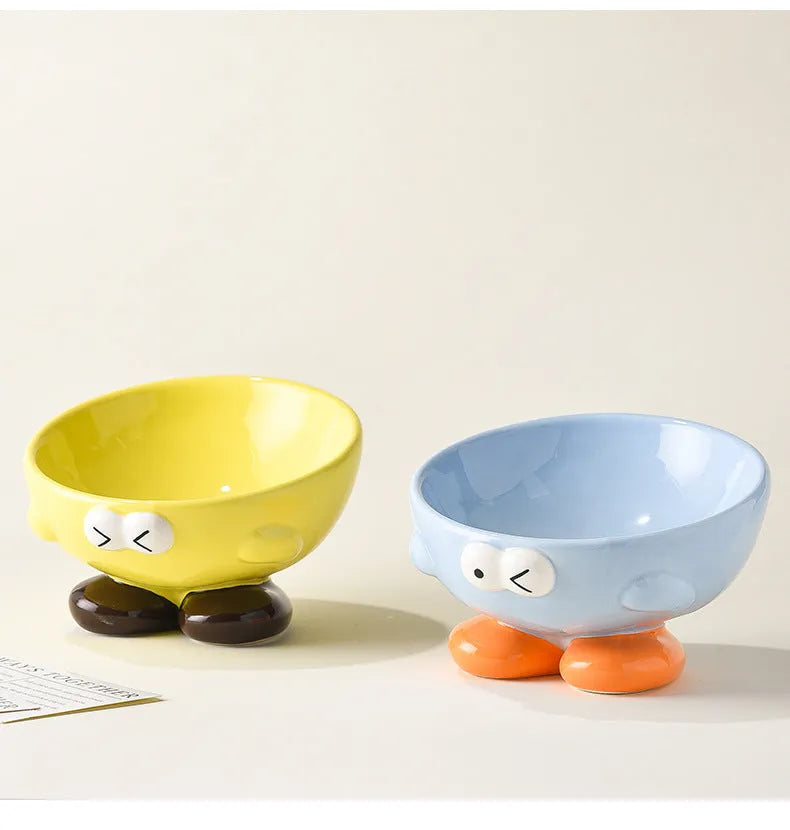 Blue and yellow ceramic slanted pet food bowls with animal face expressions for cervical spine support.
