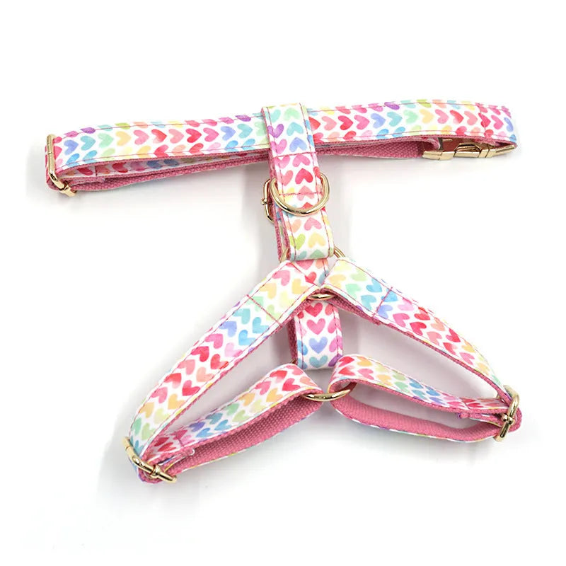 Pink dog harness with colourful heart-shaped stones and a gold-coloured buckle on a white background.