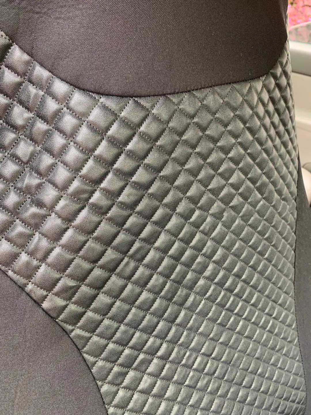 Black quilted PU car seat cover with plastic attachment hooks laid flat