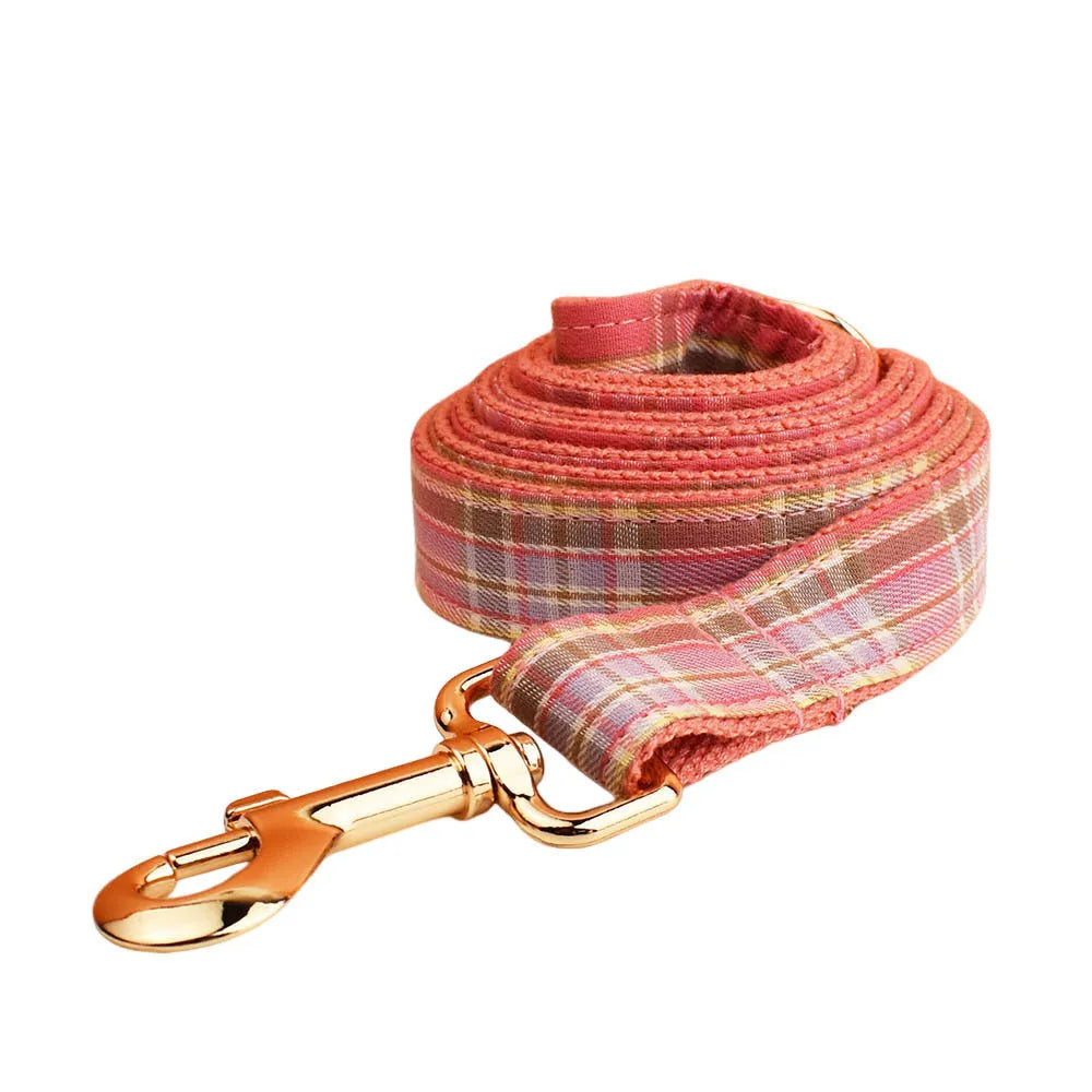 Plaid fabric dog collar, leash, bow, and vest four-piece accessory set on a white background.