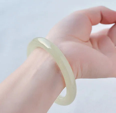 Close-up of a smooth, ice-like silk jade round bar bracelet on a wrist.