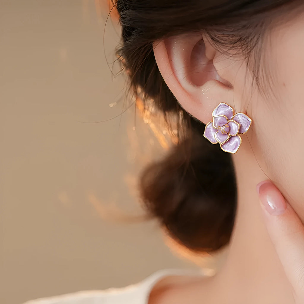 A pair of gold-plated purple flower stud earrings with an oil-spot glaze texture on a white background.