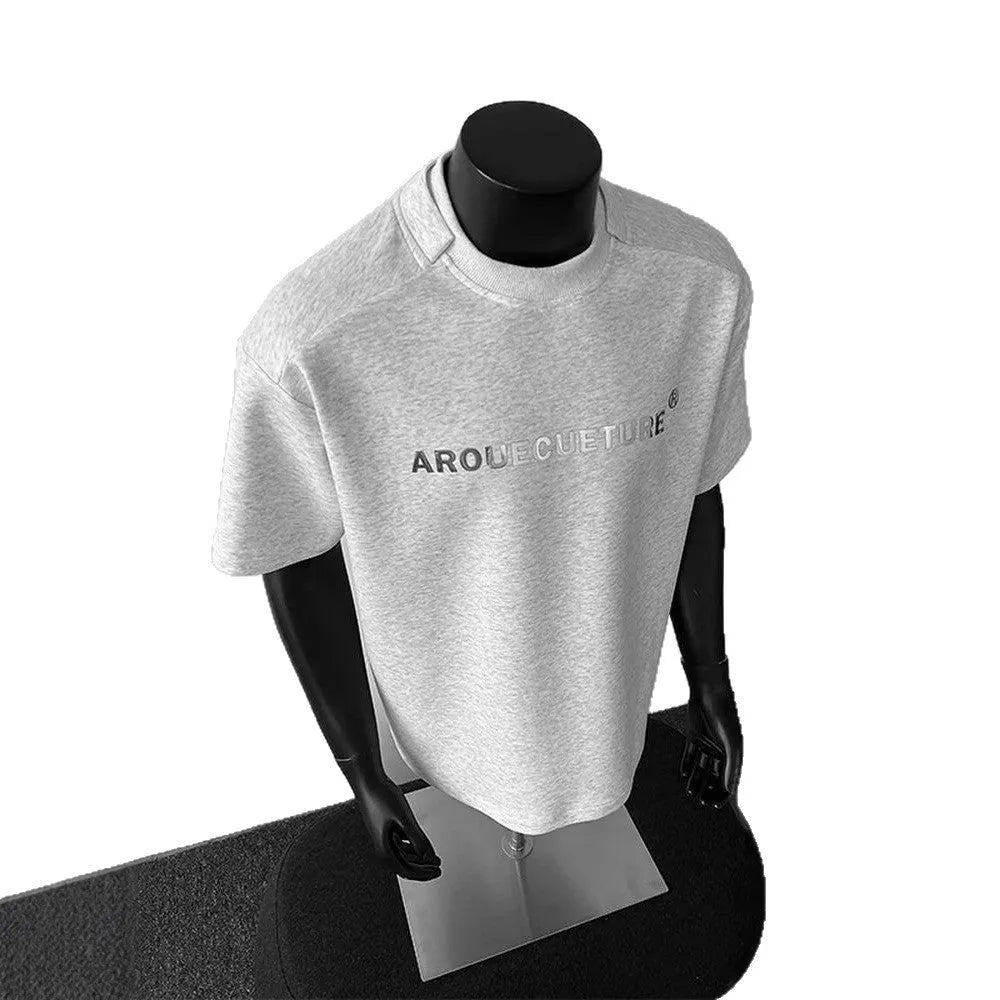 Man wearing a light grey short sleeve pullover shirt with a loose fit and black letter graphic.