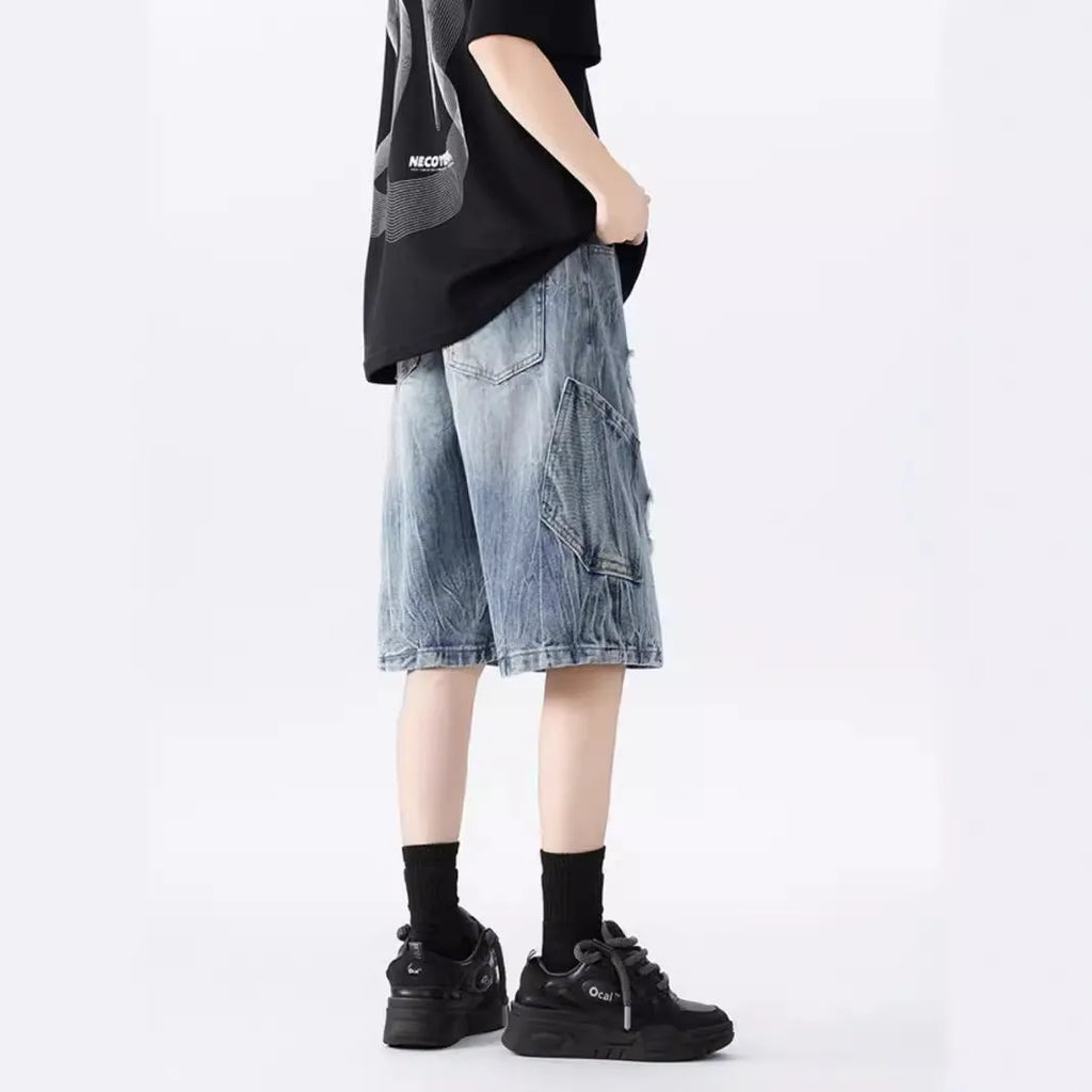 Man wearing loose-fit black denim shorts with ripped detailing and a washed vintage finish.