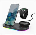Vertical 3-in-1 wireless charging stand for mobile phone, smartwatch, and headphones on a desk.