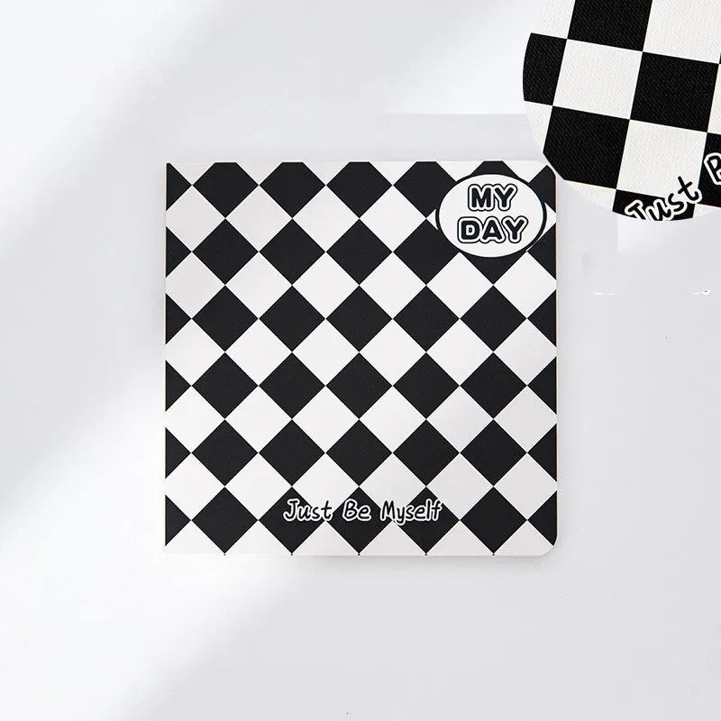 Ins style A5 grid notebook open on a desk, showing grid paper and one of twelve colourful cover designs like pineapple or checkerboard.