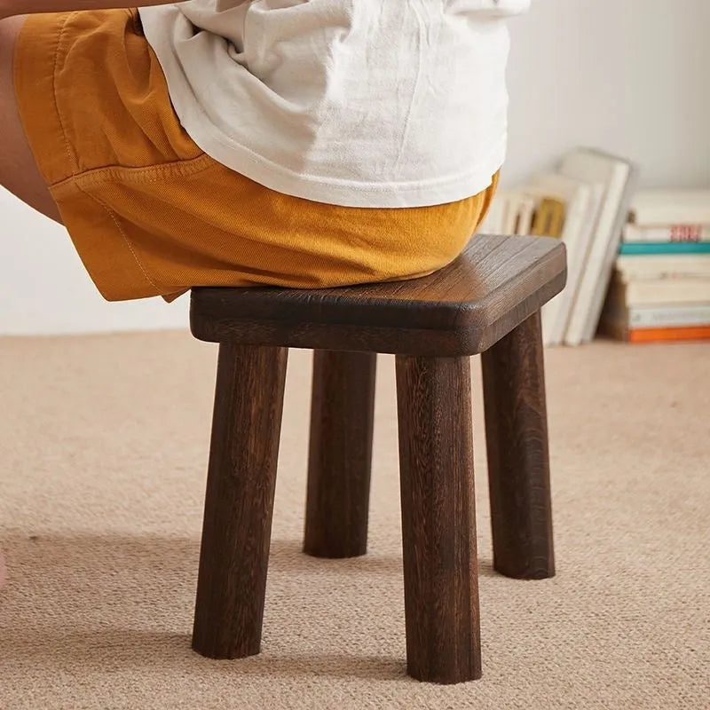 Distressed solid wood shoe stool with bracket legs in a living room setting.