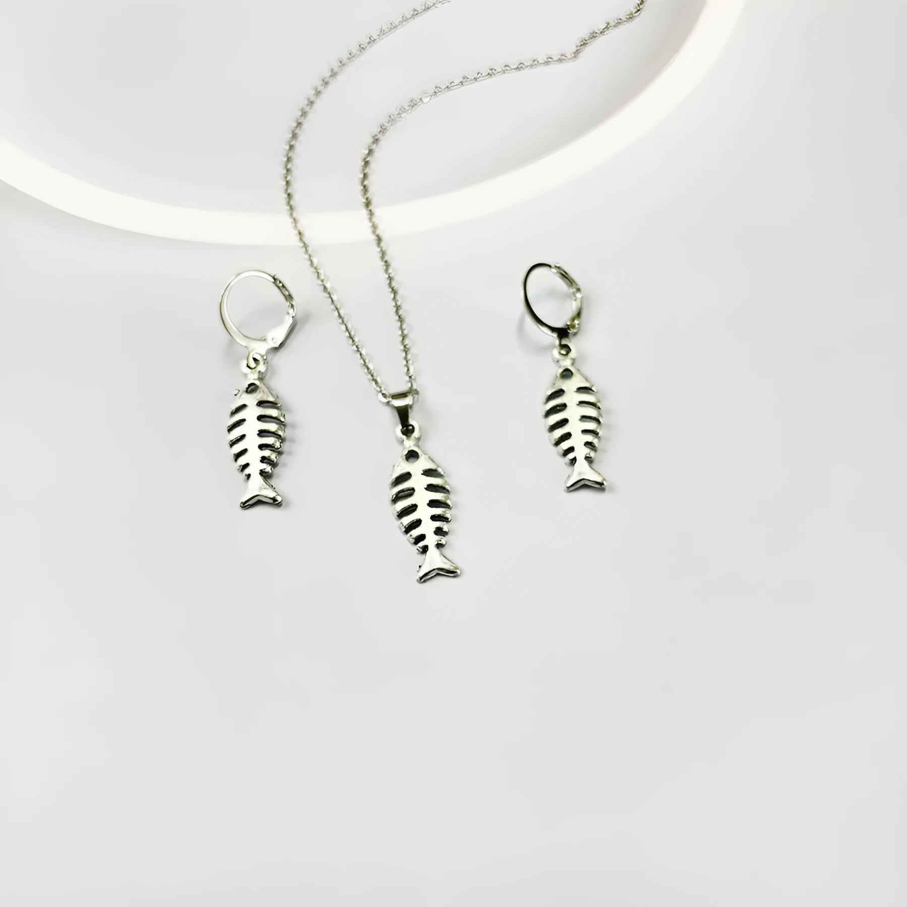 Close-up of silver fishbone pendant earrings on a white background, showing O-shaped chain detail.