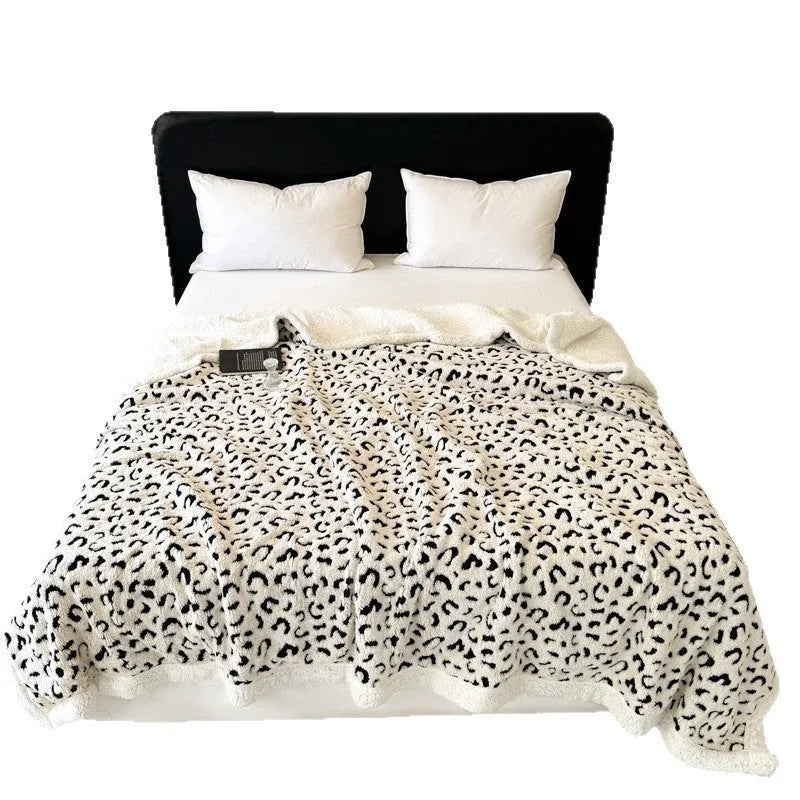 Double-layer taffeta blanket with reversible leopard jacquard print in camel colour, laid over a sofa.