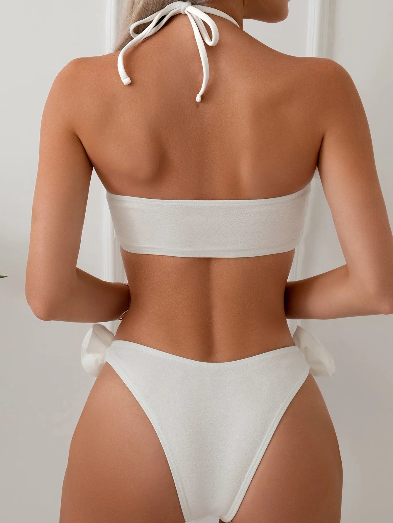 White halter bikini with lace-up front and three-dimensional floral detail on a mannequin.