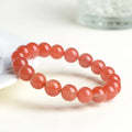 Scattered polished cherry red agate beads and elastic cord for a DIY bracelet next to an assembled single-strand bracelet.